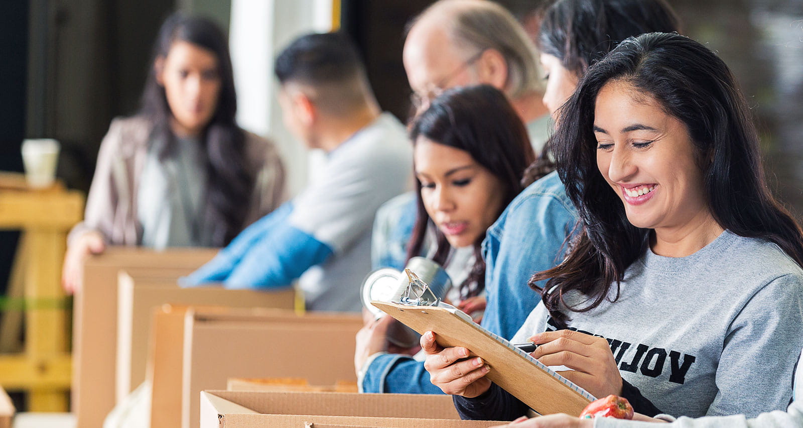 A diverse group of volunteers packing cardboard boxes full of donated food in a charity food bank