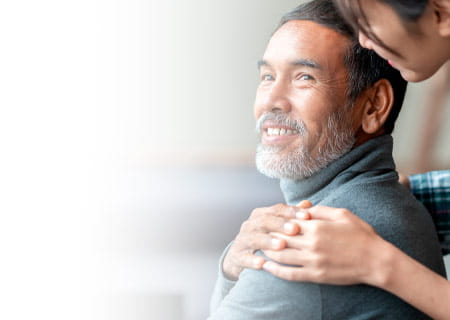 A smiling man being hugged by his wife