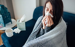 A woman wrapped in a blanket using a tissue