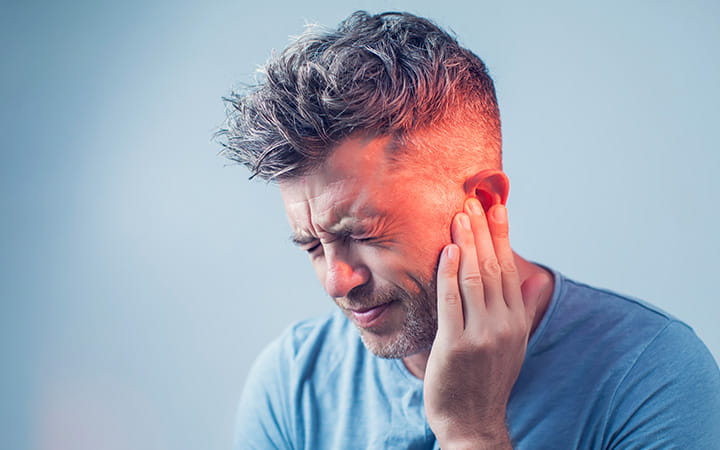 grimacing man with fingertips of one hand on his ear