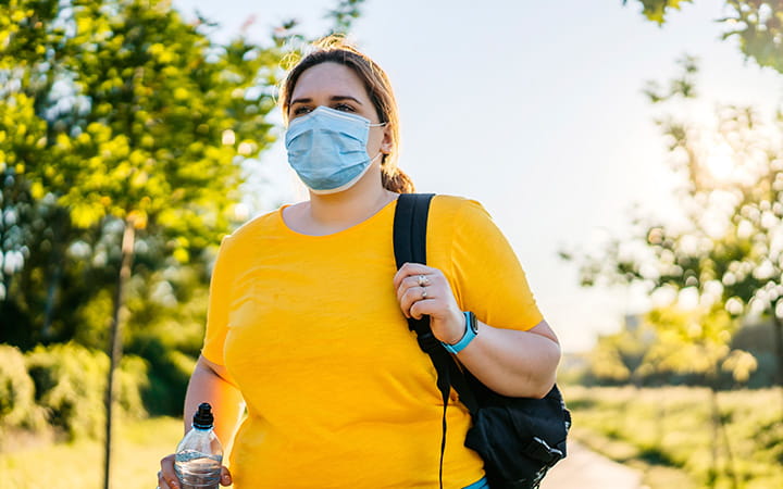 Overweight woman walking with mask and bottled water