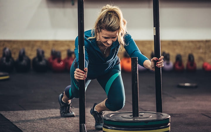 woman pushing weight laden sled at the gym