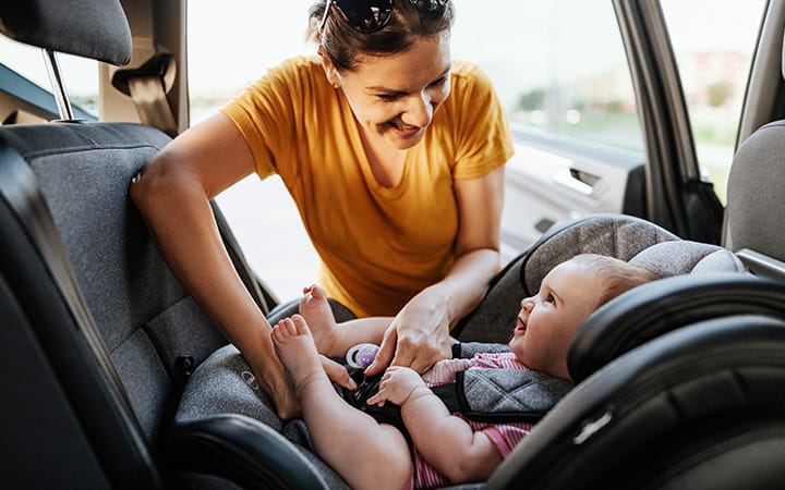 smiling mom buckles in infant into rear-facing car seat