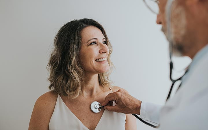Doctor listening to mature adult female patient's heart with stethoscope