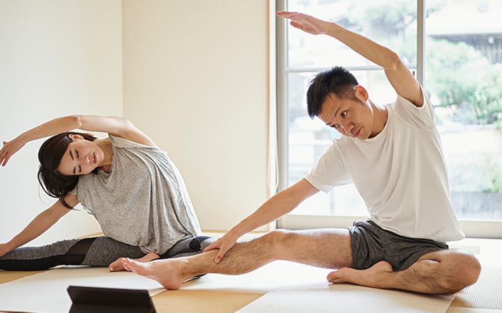man and woman doing seated side stretches at home