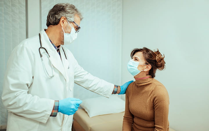 male doctor in mask with hand on the shoulder of seated woman in mask