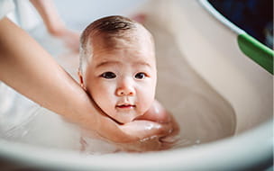 small baby in bathtub held by adult arms