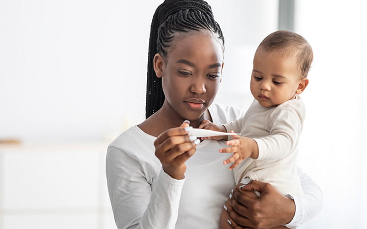 mother holding a baby and looking at a thermometer
