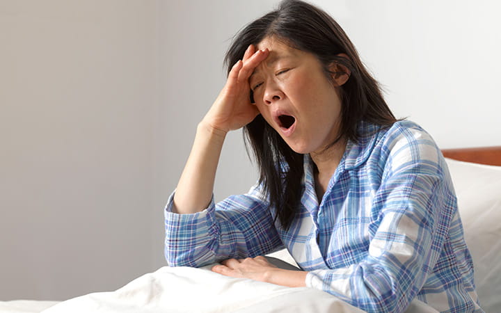 woman in bed yawning with hand to forehead