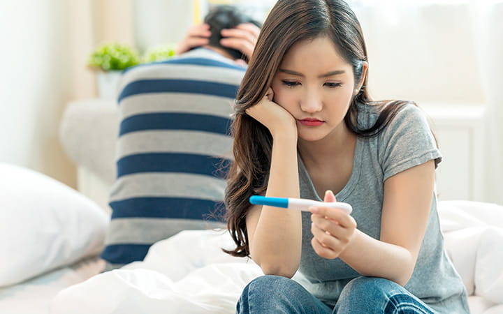 woman looking at home pregnancy test with man next to her with head in hands