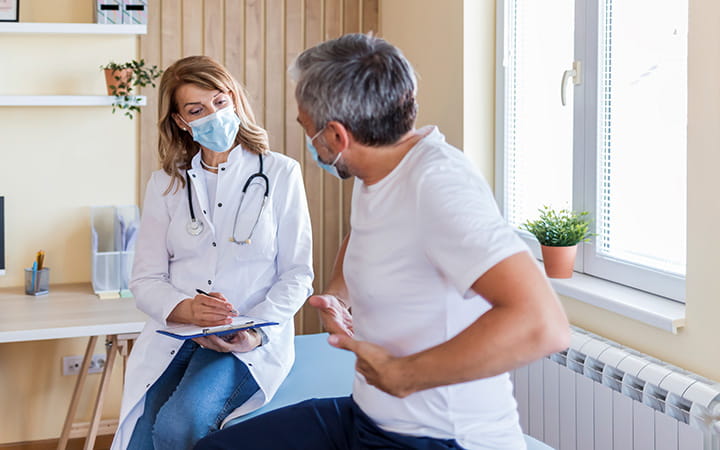 man with hands on abdomen talking with clinician in mask
