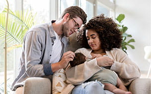 A young woman breastfeeds her infant son as her husband smiles at the baby