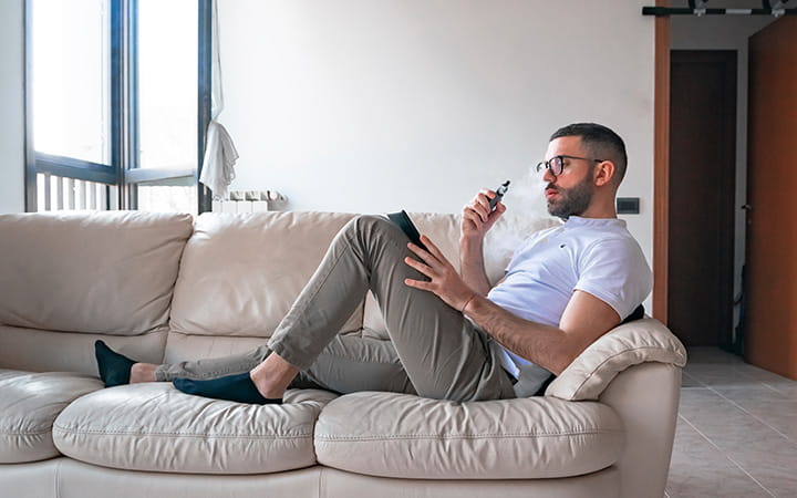 A man smoking while using digital tablet on sofa at home