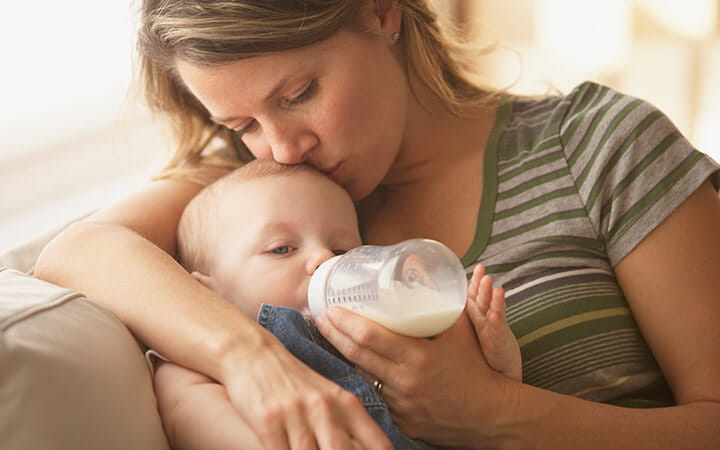 Mother feeding baby with bottle on sofa