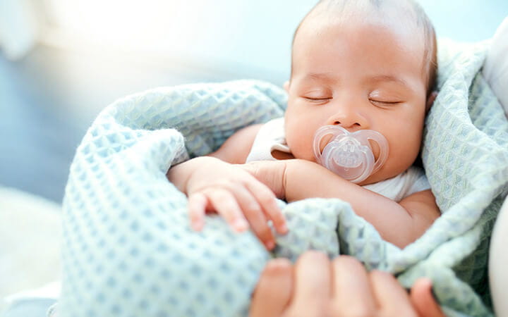 An adorable baby boy sleeping in his mother's arms