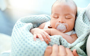 An adorable baby boy sleeping in his mother's arms
