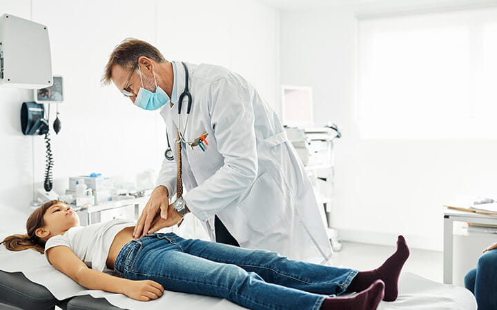Male pediatrician pressing stomach of girl during checkup