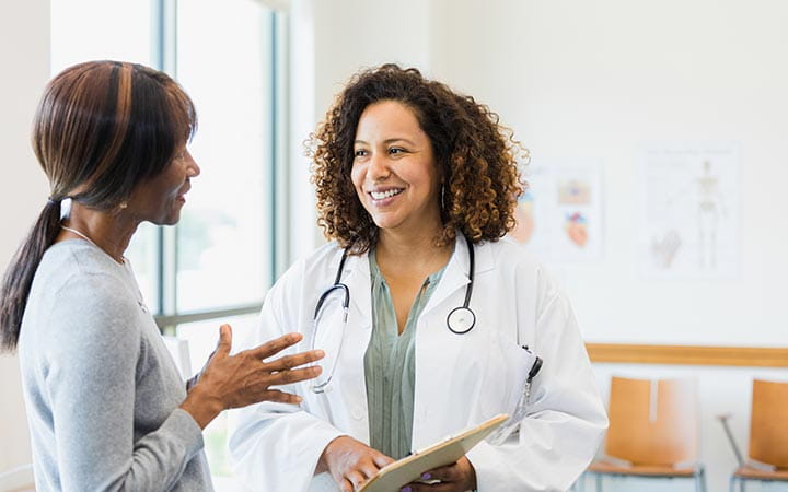 Mid adult female doctor smiles as she listens to the mature adult female patient