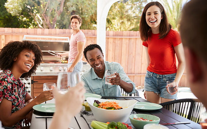 Young adult friends sitting outdoors for lunchtime barbecue