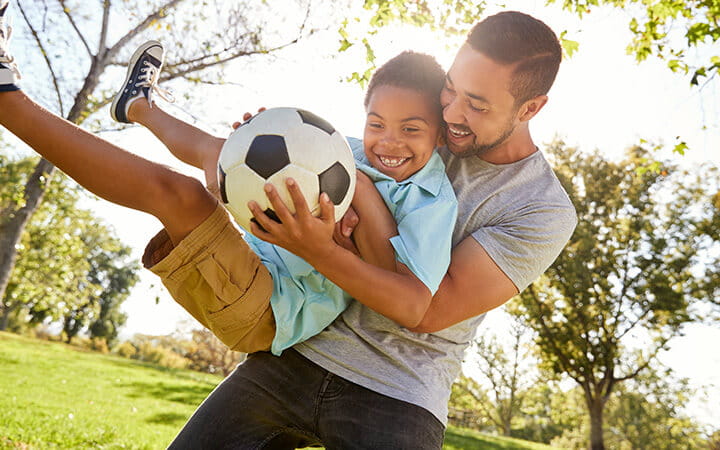 Father and son playing soccer in park together