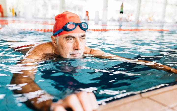 A senior man relaxing in water by edge of a swimming pool