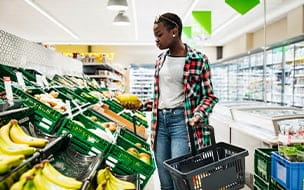 A young woman holding a basket and a melon while shopping for fruit at her local supermarket