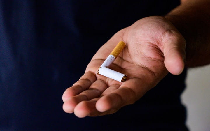 An outstretched hand holding a broken cigarette