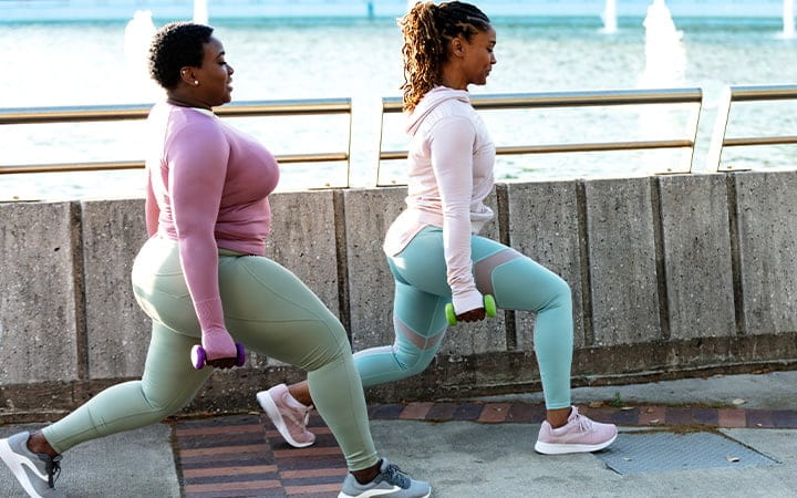 Two African-American woman exercising together in a city park, by a large fountain on a city waterfront