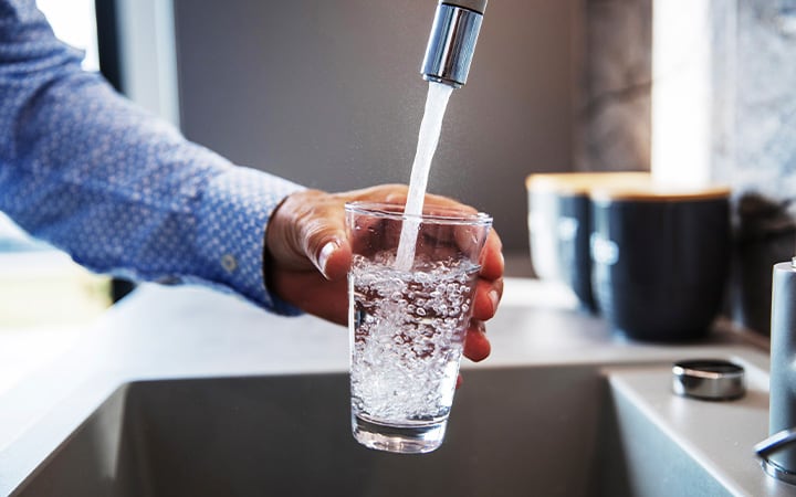 Mature male hand pouring a glass of water from tap in the kitchen sink