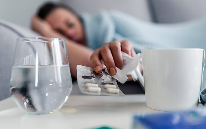 A woman reaching for a packet of medicine next to glass of water on her nightstand