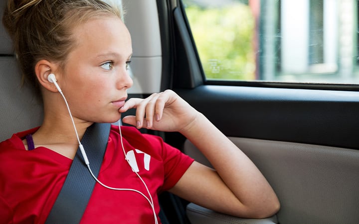 A young girl listening to music on smart phone while looking out the window of a car
