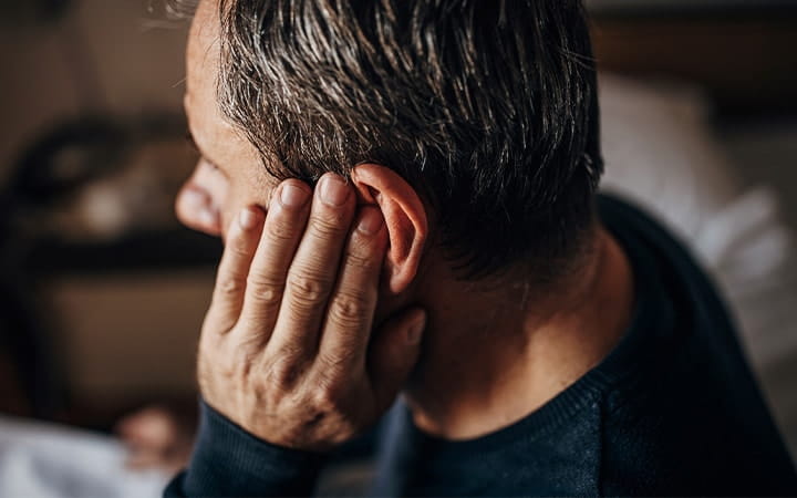 An older man holding his left ear