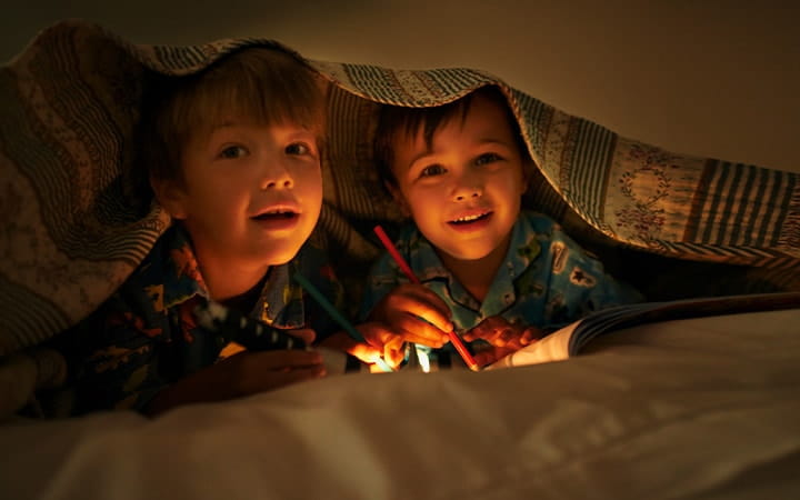 Two boys under the covers with a flashlight and coloring book