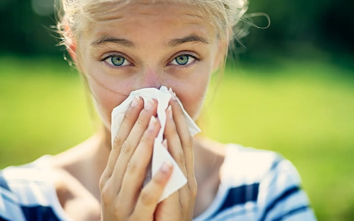 A teenage girl with allergies blowing her nose on a summer day