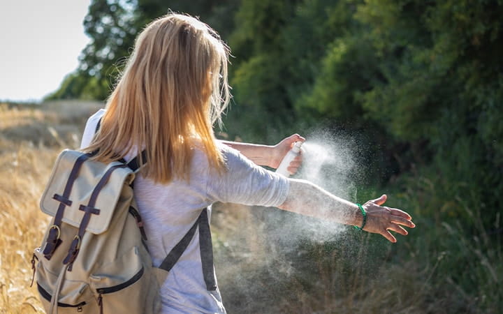 Woman tourist applying mosquito repellent on hand during hike in nature