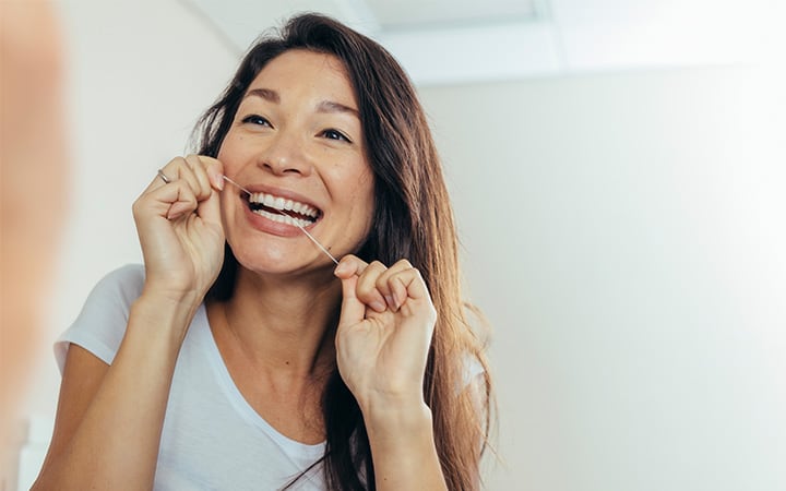Woman looking in the bathroom mirror and using dental floss to clean her teeth