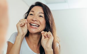 Woman looking in the bathroom mirror and using dental floss to clean her teeth