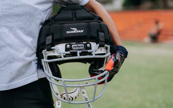 A boy holds a football helmet equipped with a Guardian Cap