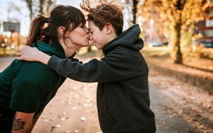 Young woman kissing and embracing her son outdoor, standing face to face on sunny day