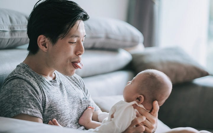 A young father bonding and playing with his infant son in their living room