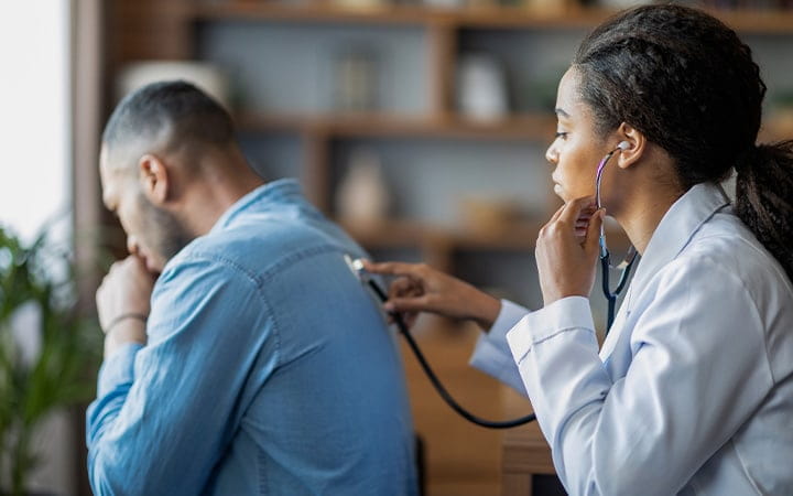 A female doctor checking the lungs of a male patient with a stethoscope