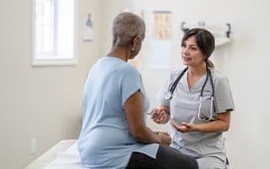 A middle-aged woman sits up on an exam table for a check-up with a nurse facing her