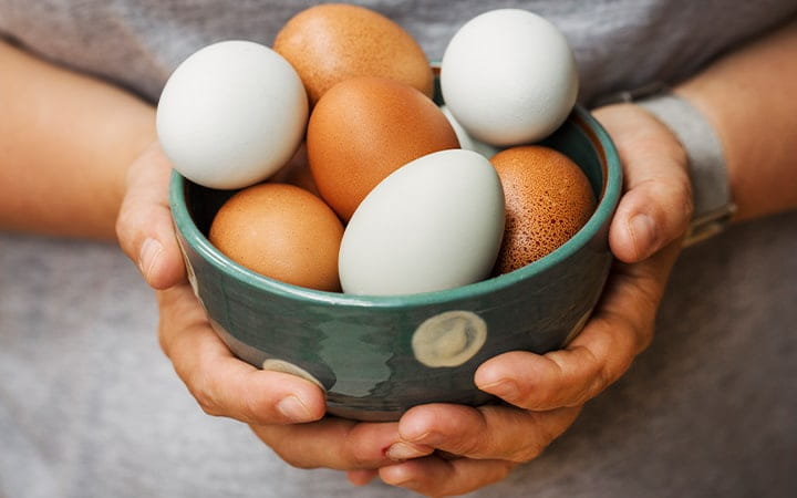 A woman holding a bowl with fresh brown and white eggs