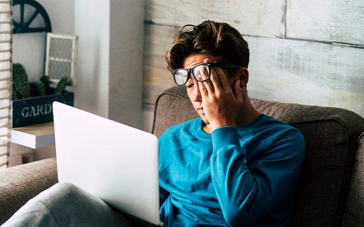 A tired teenager at home studying with a personal laptop computer