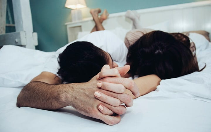 man and woman hold hands in bed