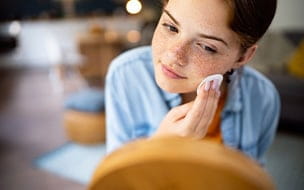 Teenage girl cleaning her face with cotton pad in front of the mirror