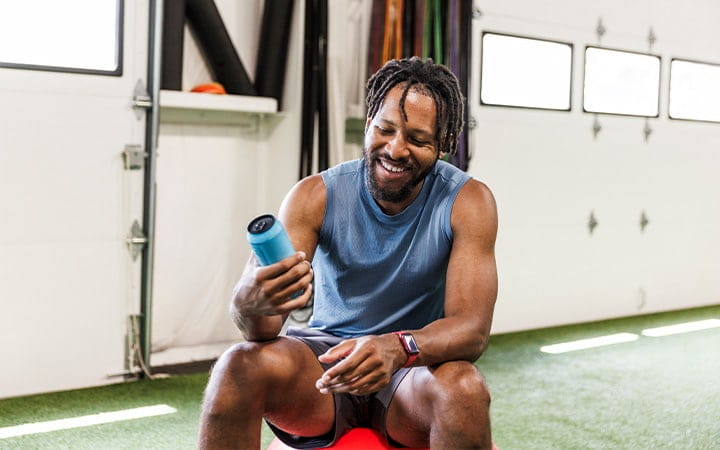 A smiling man holding an energy drink while sitting at health club