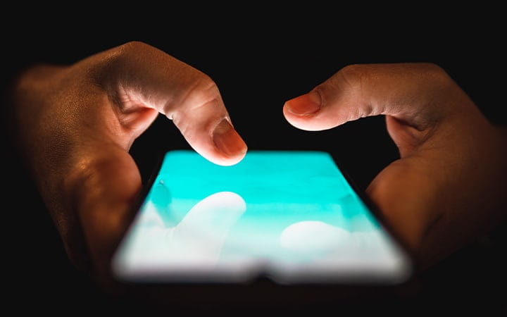 A person scrolling on a cell phone in the dark