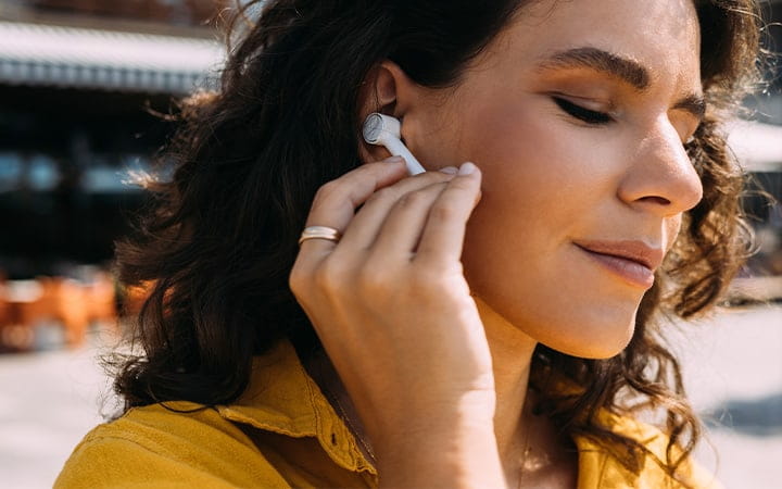A smiling woman wearing earbuds while enjoying listening to music