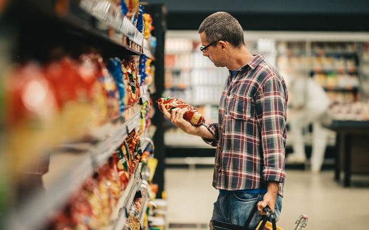 Man standing in a supermarket aisle and reading the label on a bag of pasta while grocery shopping